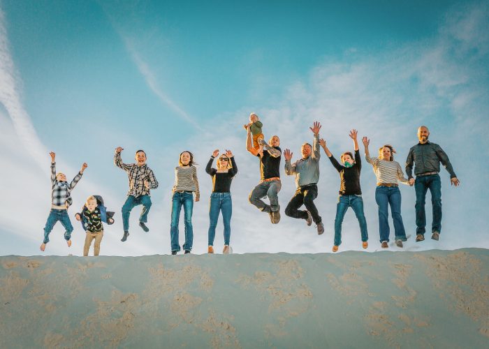 A group of people jumping simultaneously on a sand dune under a clear blue sky.